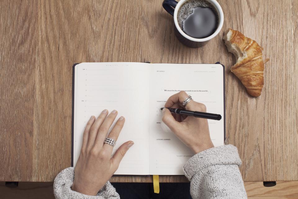 Manos escribiendo en un diario junto a un café